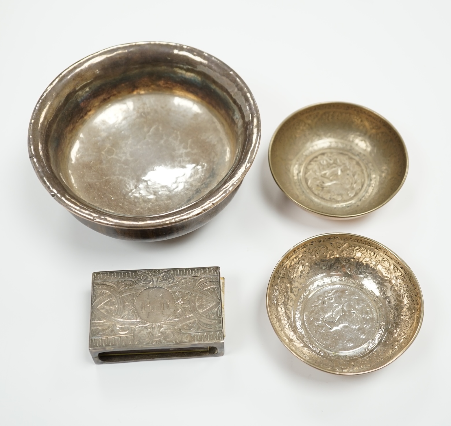 A Tibetan white metal mounted cup, two coin inset dishes and a silver matchbox holder, largest 11.5cm diameter